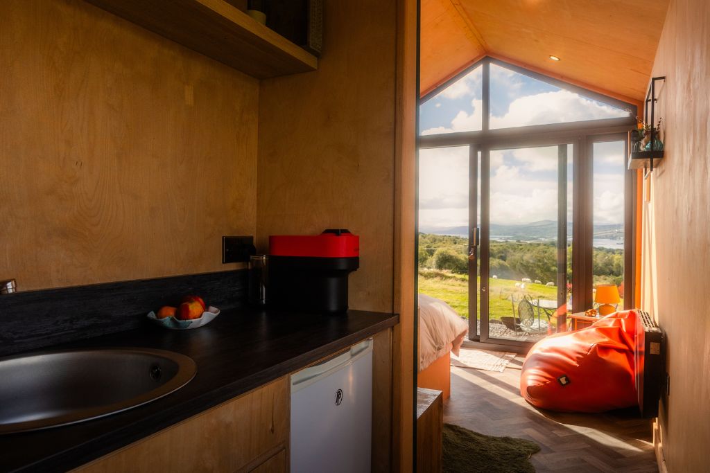 Cabin kitchenette with coffee machine and a view through open doors to Kenmare Bay
