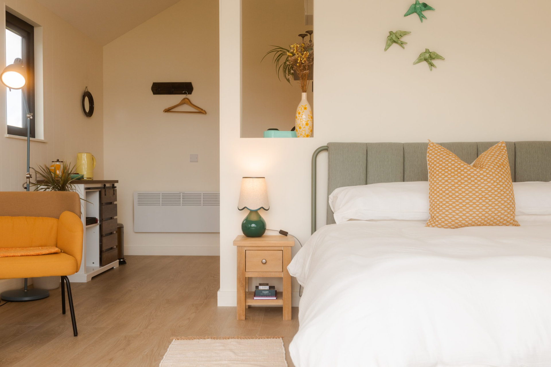 Beithe bedroom with a sage headboard, crisp white linen and a warm bedside lamp