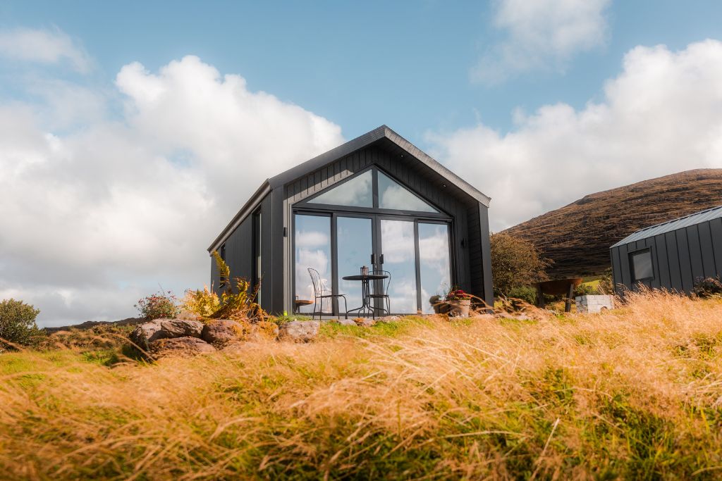 Beithe cabin exterior in dark timber with a glass gable above golden grasses