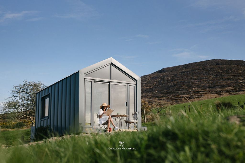 Dairach cabin exterior with a glass gable and a guest reading at the bistro table