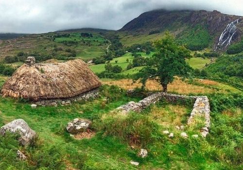 Thatched stone cottage in the green Gleninchaquin valley with a waterfall on the mountainside behind