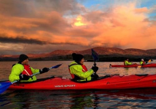 Two people paddling kayaks on Kenmare Bay under a red sunset sky